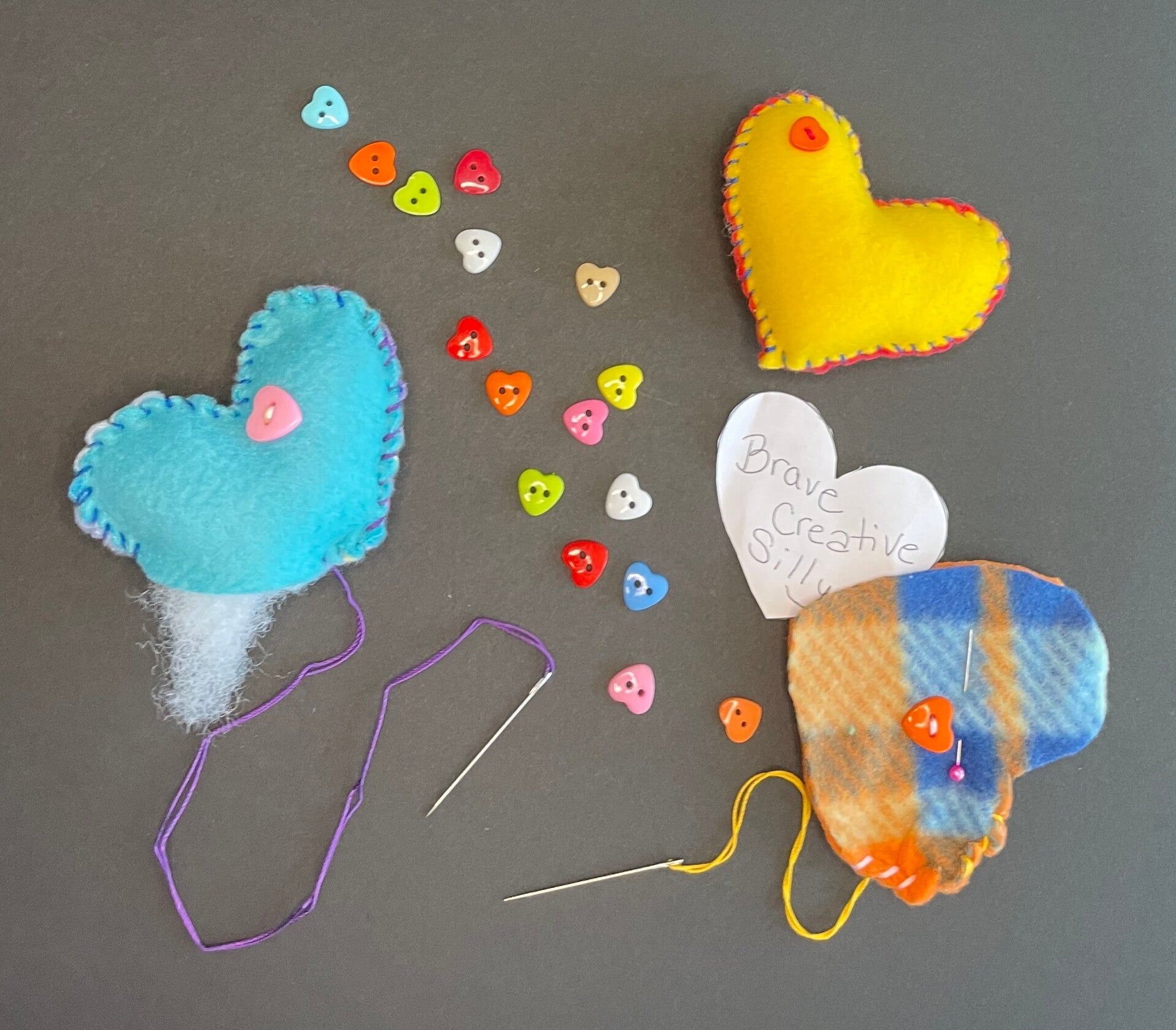 Hand-sewing supplies arranged for a beginner sewing workshop, including felt hearts, colorful decorations, thread, needles, and a plush monster.