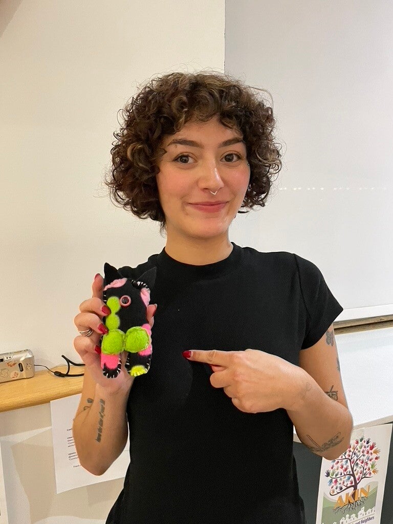 Workshop participant smiling and holding a colorful handmade monster during an AKIN community fundraiser.