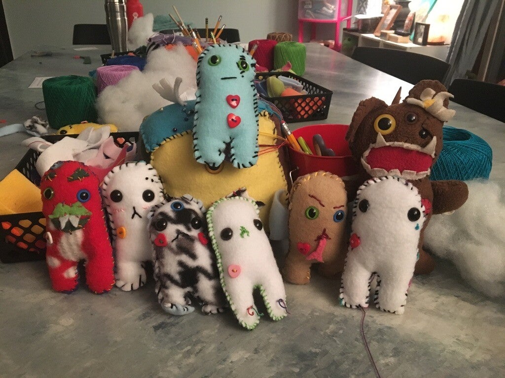 Collection of colorful handmade plush monsters displayed on a table.
