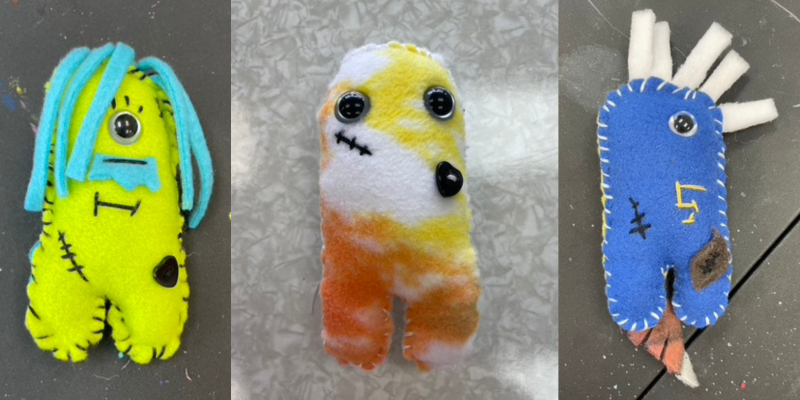 Three colorful handmade plush monsters displayed side by side, each with unique fabric, button eyes, and stitched details.