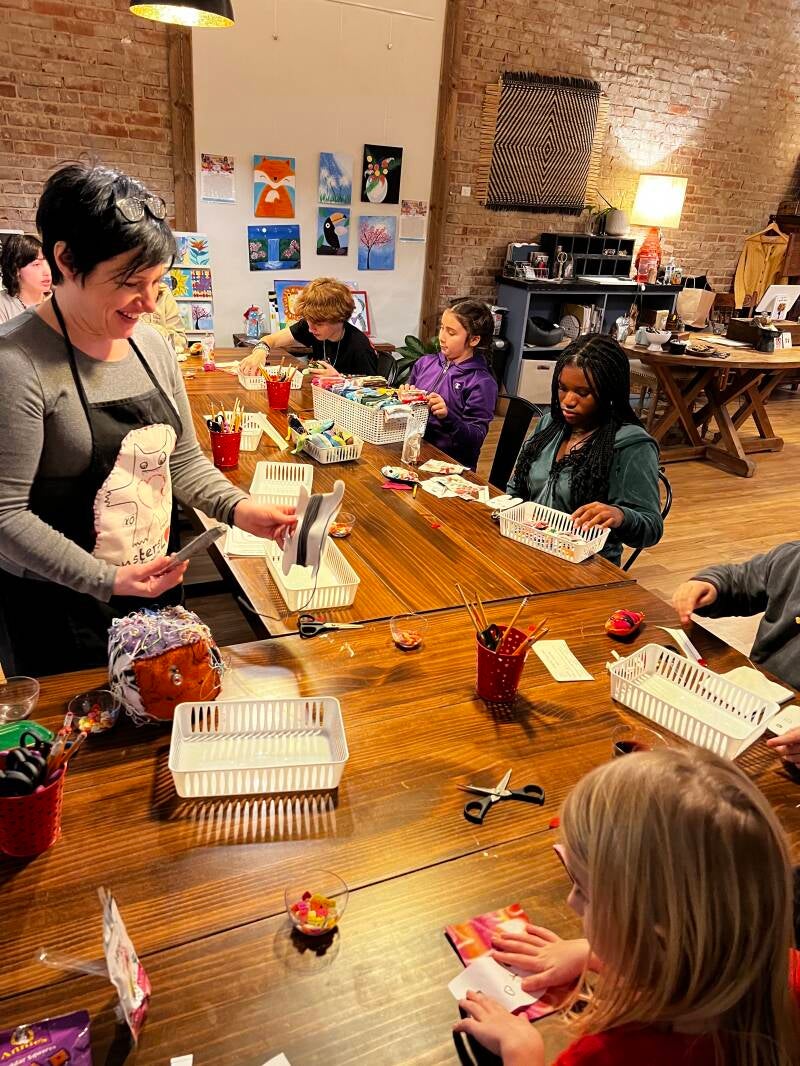 People gathered around a table with colorful fabric, stuffing, and craft supplies.