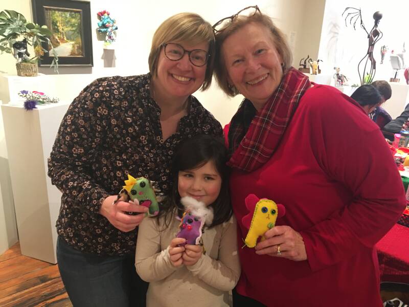 Two adults and a child smiling while holding handmade plush monsters.
