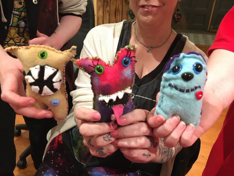 Person holding three colorful handmade plush monsters.