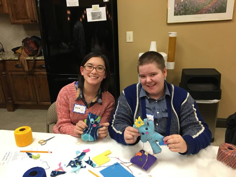 Two people smiling while holding handmade plush monsters.