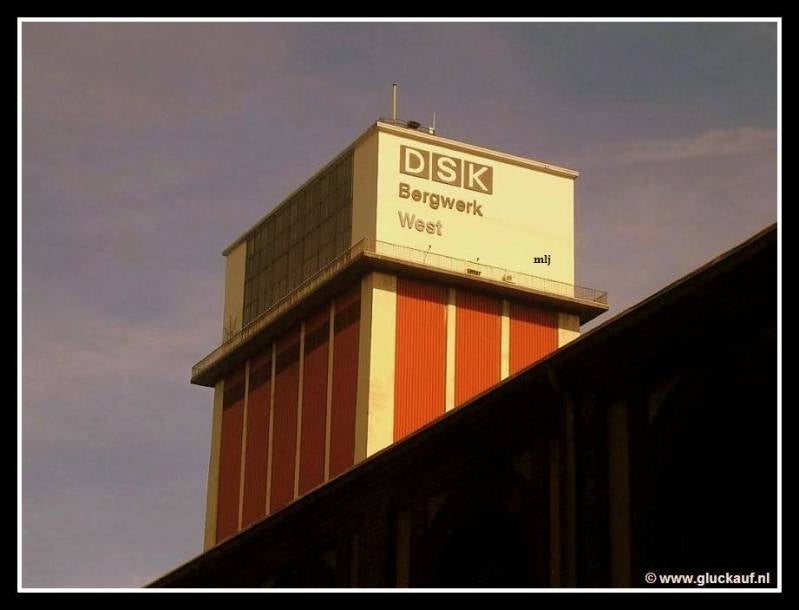 Op de voorgrond een van de prachtige gebouwen van de mijn en op de achtergrond met de tekst Bergwerk West erop, de materiaalschacht. © www.gluckauf.nl