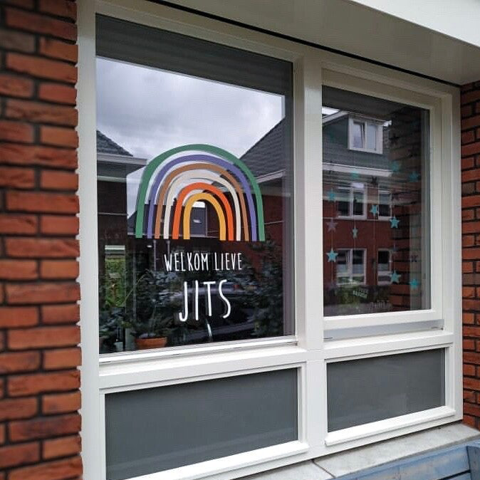 Geboortesticker met naam en regenboog op het raam
