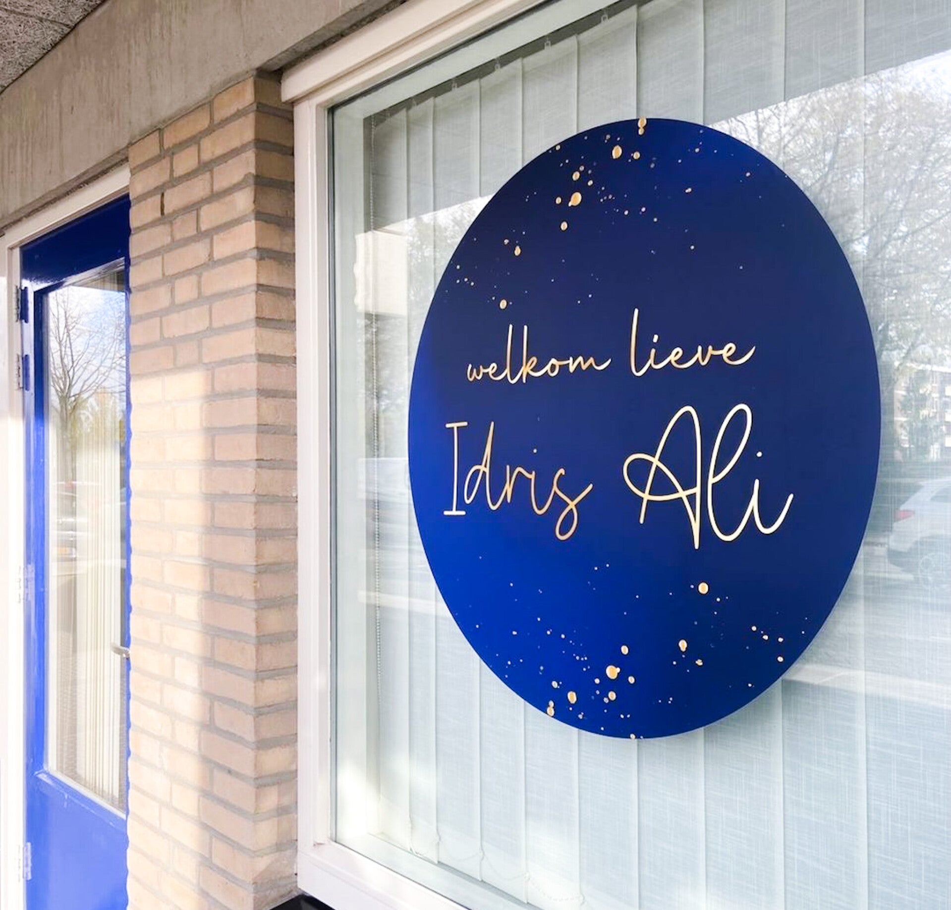 Blauwe geboortesticker met naam in goudkleurige letters op het raam