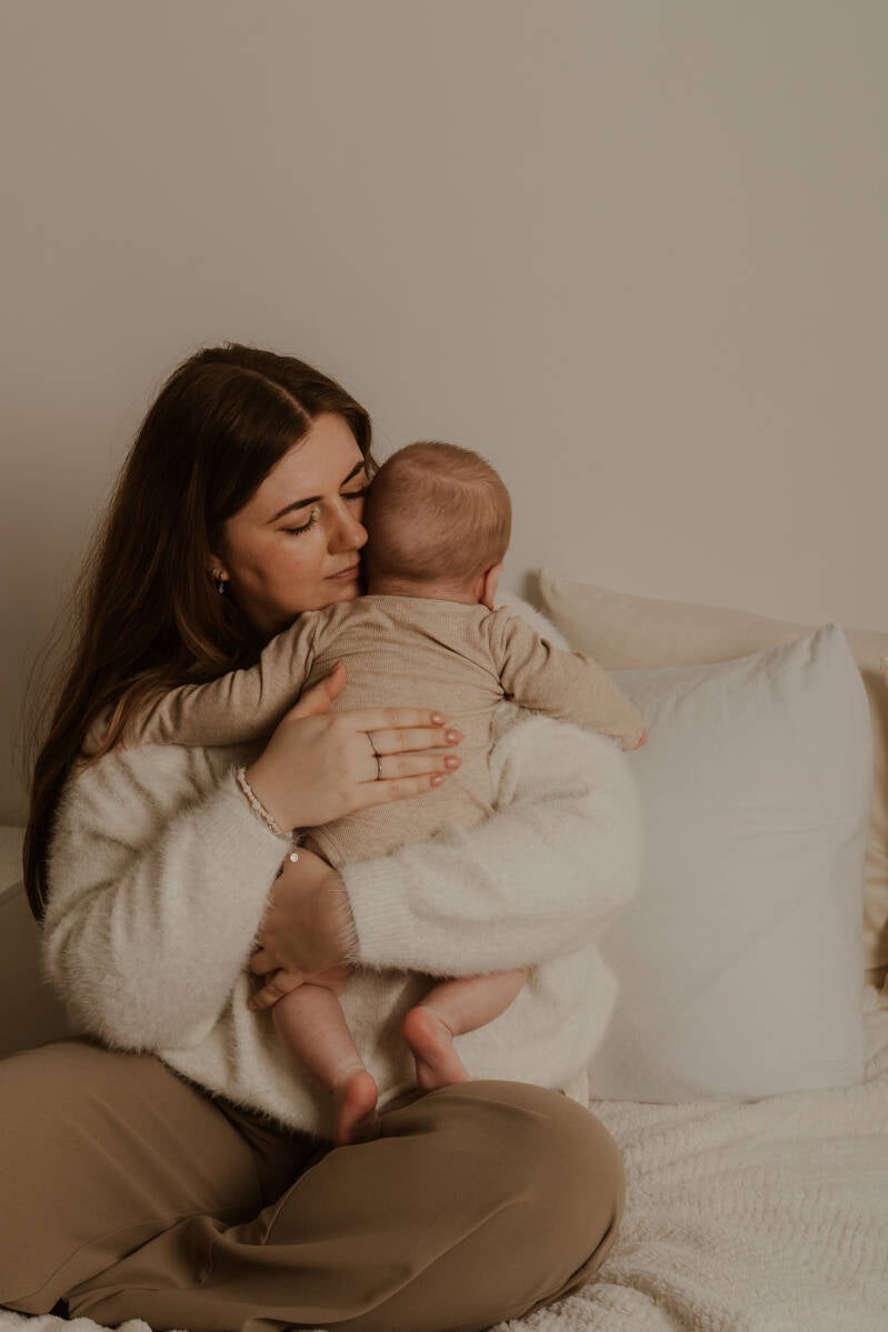 mama met baby tegen zich aan knuffelend zittend op bed