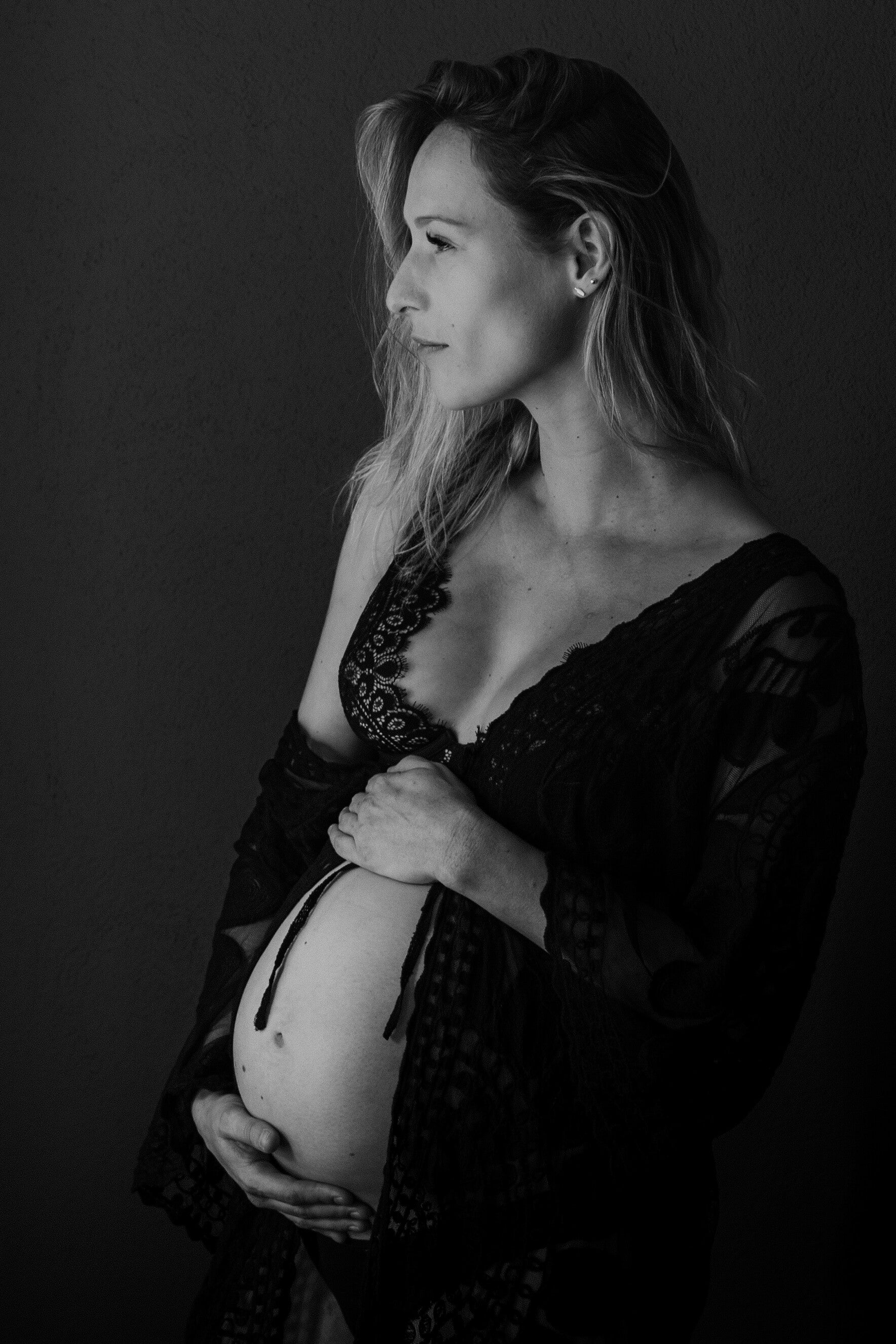 zwart wit foto van zwangere vrouw strak voor zich uit kijkend met haar hand om haar buik