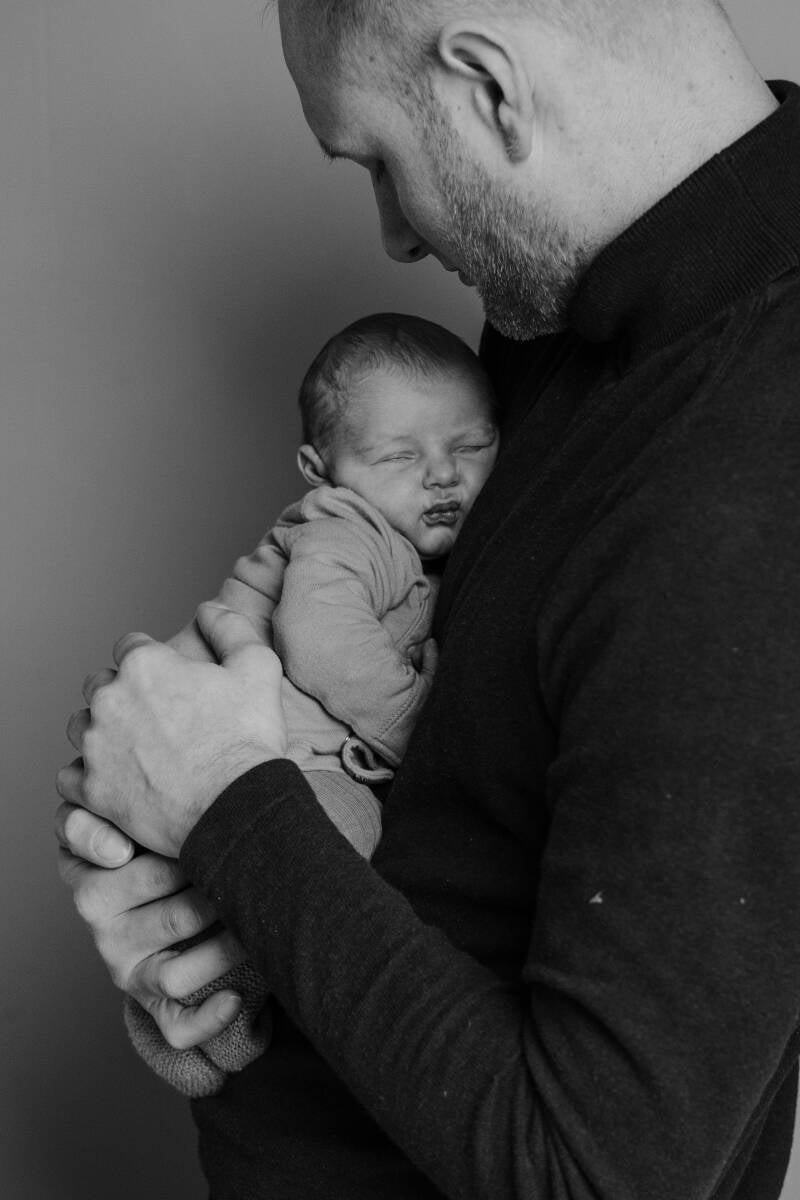 pasgeboren baby hangt opgekruld tegen borst van papa