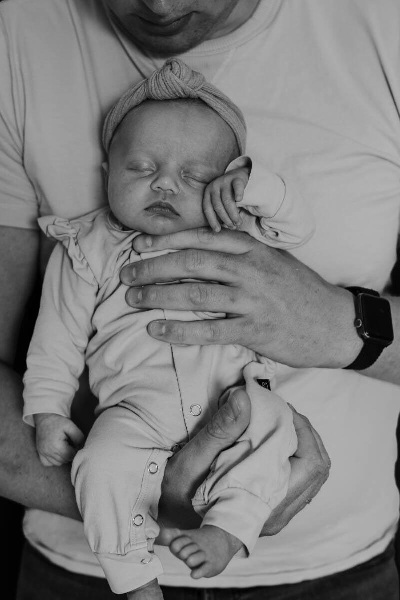 baby van voren gefotografeerd hangend tegen buik van papa