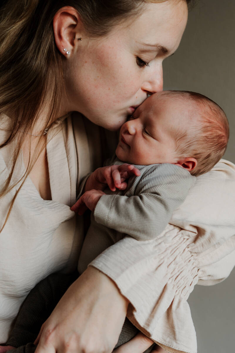 mama geeft pasgeboren baby kus op voorhoofd