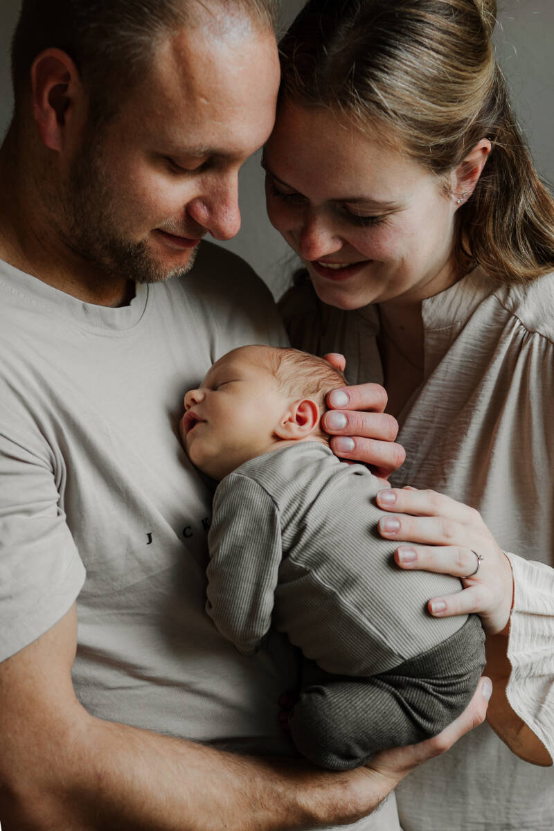 pasgeboren baby slapend tegen borst van papa met handen van beide ouders eromheen