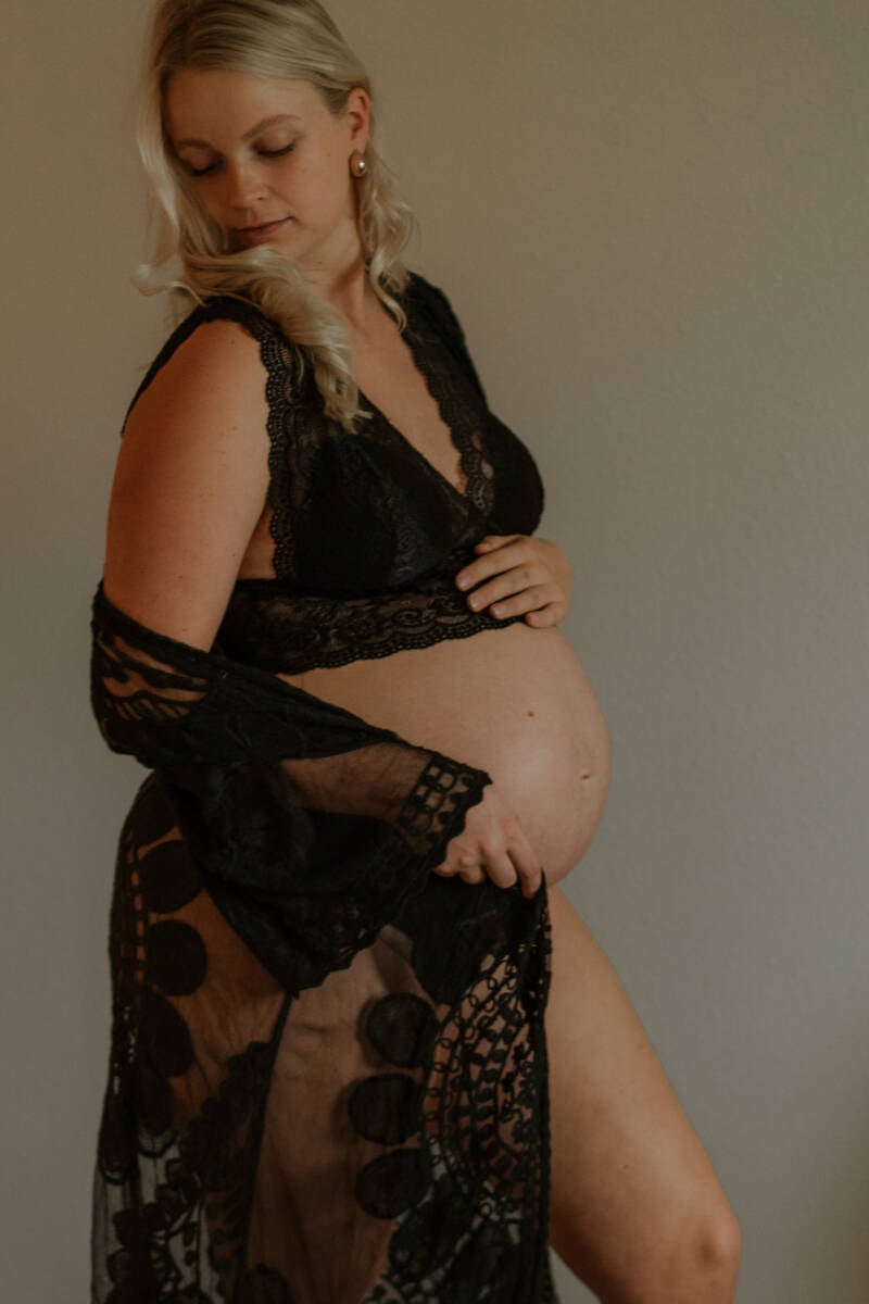 kleurfoto van zwangere vrouw zwierend in kaftan met zwarte lingerie