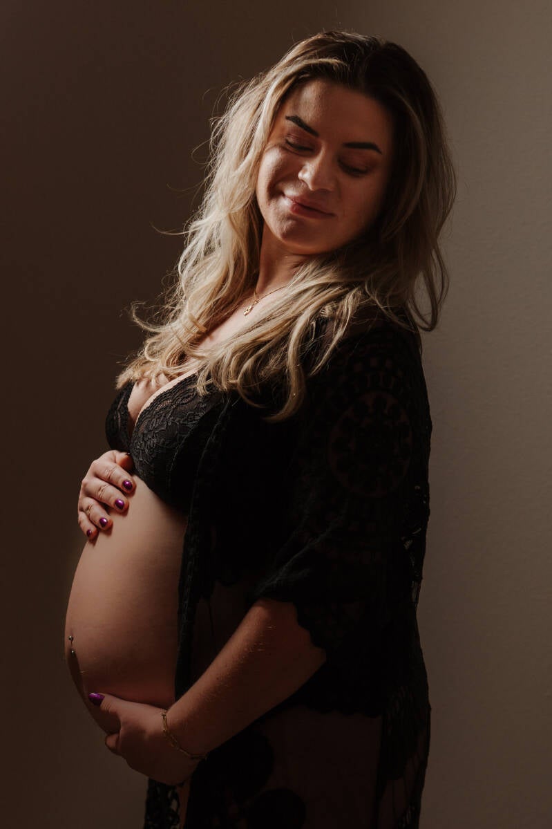 kleurenfoto van een zwangere vrouw over schouder kijkend met zwarte lingerie