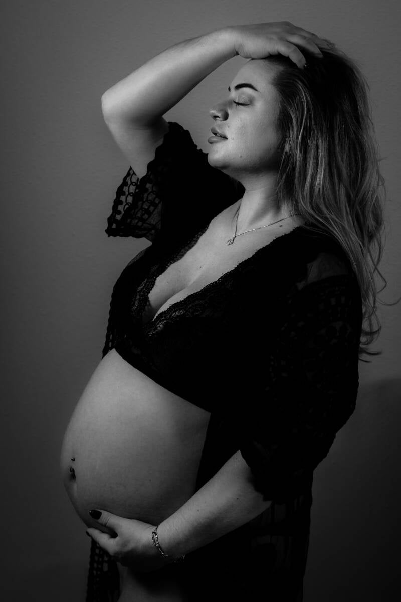 zwart wit foto van zwangere vrouw poserend in lingerie met 1 hand in haar