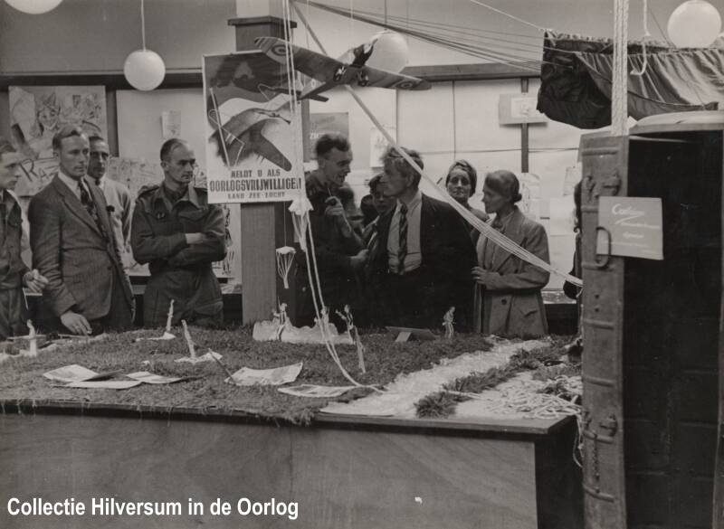 Het voormalige verzet geeft informatie over droppings. Rechts is een droppingscontainer tentoongesteld. Hier zaten wapens in die gedropt werden door de geallieerden. Te zien zijn o.a. Bob de Geus, Joop Bijl en Gé Verheul. Collectie Hilversum in de Oorlog