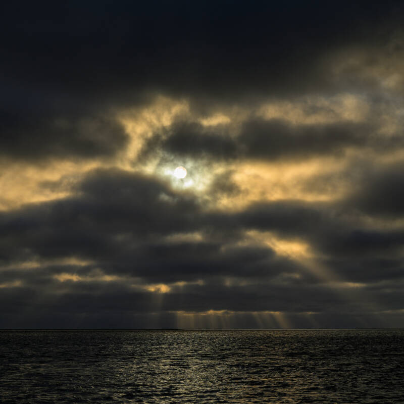 Zonnestralen door de wolken net na zonsopkomst boven de Noordzee