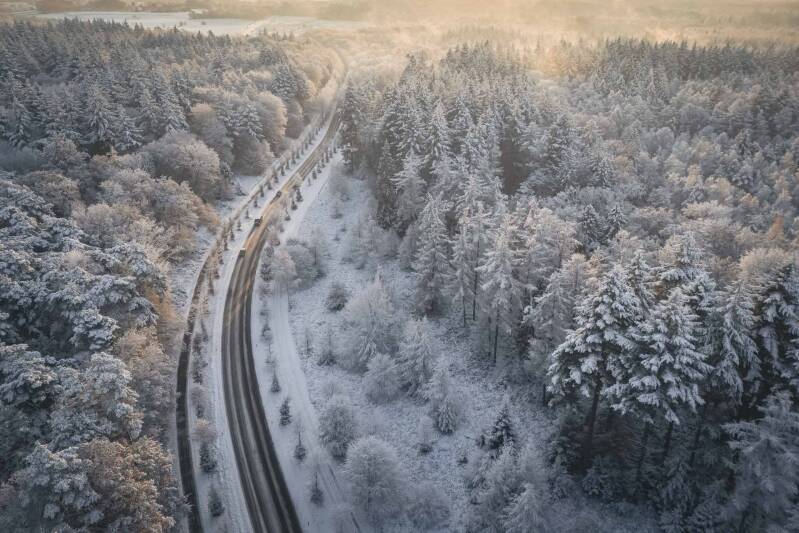 Aerial landscap image of a forest road in full snow with 3 cars on the road.