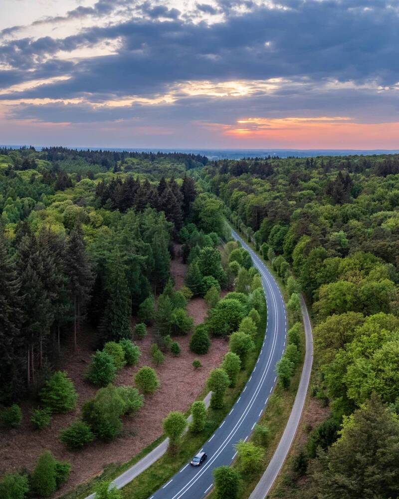 Drone photo of a curving forest road in spring below a colorful sunset cloudy sky