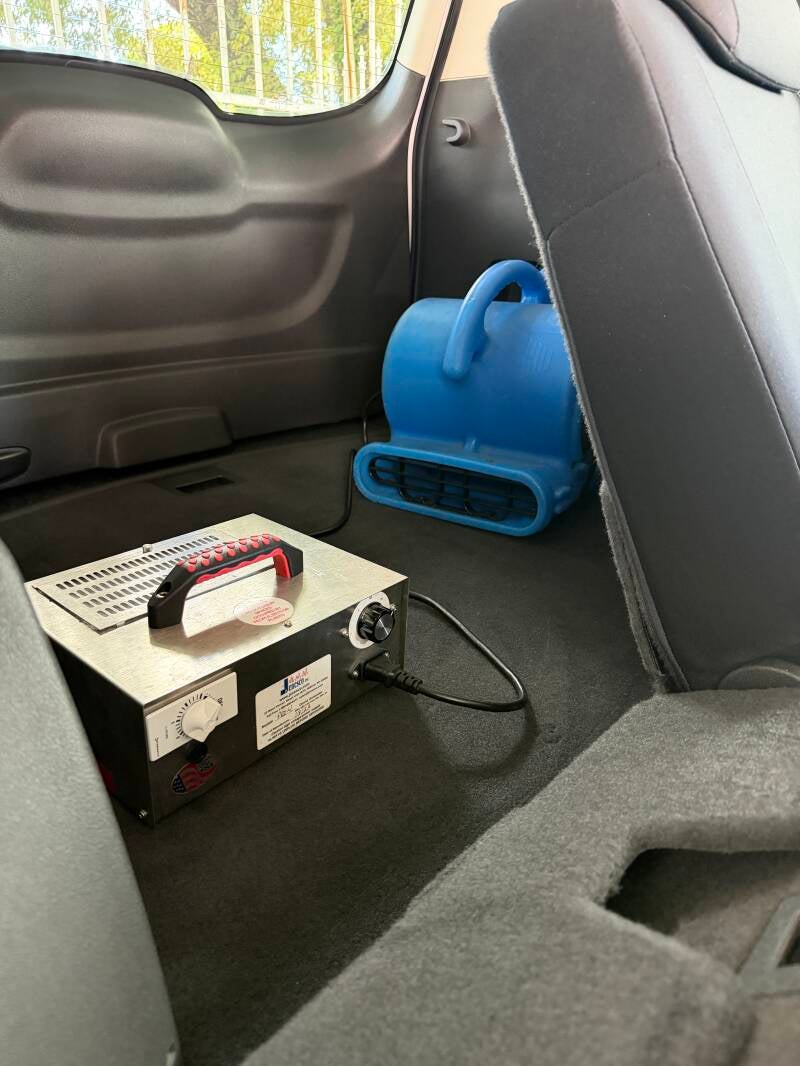 Ozone generator and air mover operating inside a vehicle during a professional odor-removal treatment.
