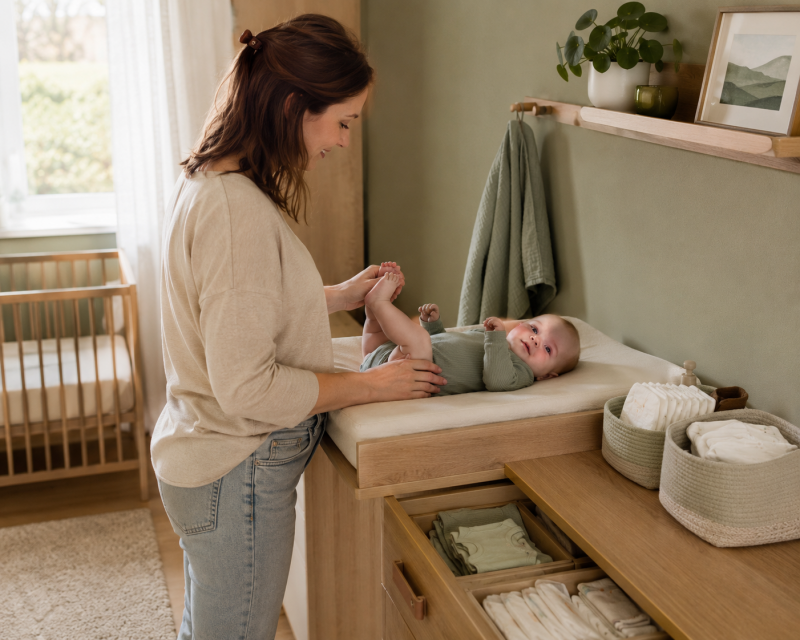 Mama wickelt ihr Baby auf einer kleinen Wickelkommode mit Windeln und Wechselkleidung in Reichweite