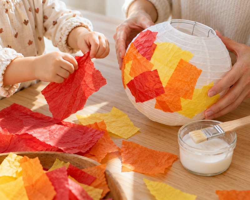 Kleinkind und Mutter gestalten gemeinsam eine Laterne mit bunten Papierschnipseln