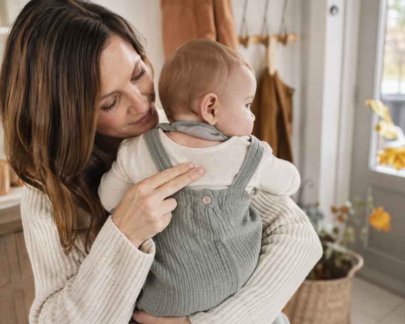 Mutter kontrolliert mit zwei Fingern den Nacken ihres Babys, um die Temperatur der Kleidung zu prüfen.