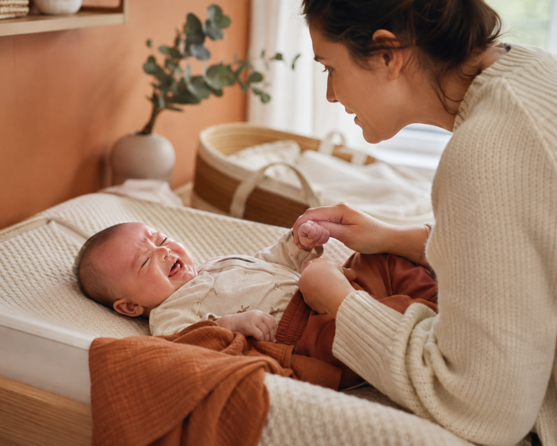 Mutter zieht ihrem weinenden Baby vorsichtig einen Wickelbody an