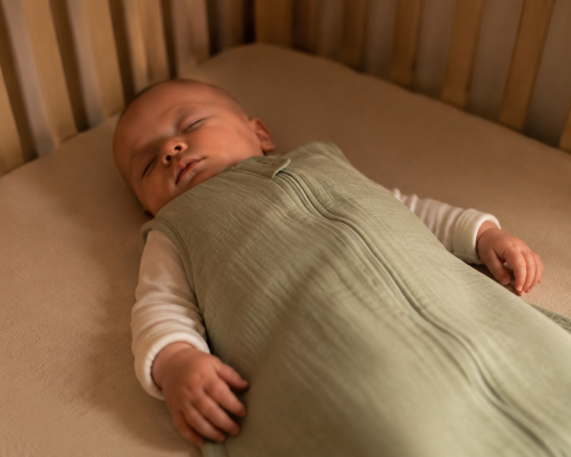 Baby schläft bei 18 Grad im Schlafsack auf dem Rücken in einem sicher eingerichteten Babybett.