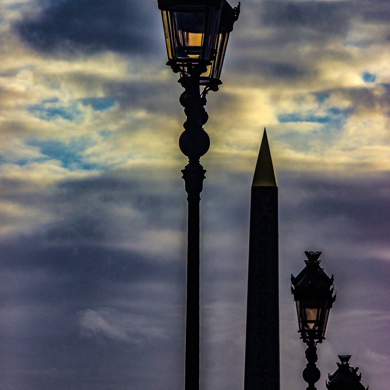 Lampioni parigini in controluce al tramonto con cielo nuvoloso, tra linee verticali e sfumature di luce