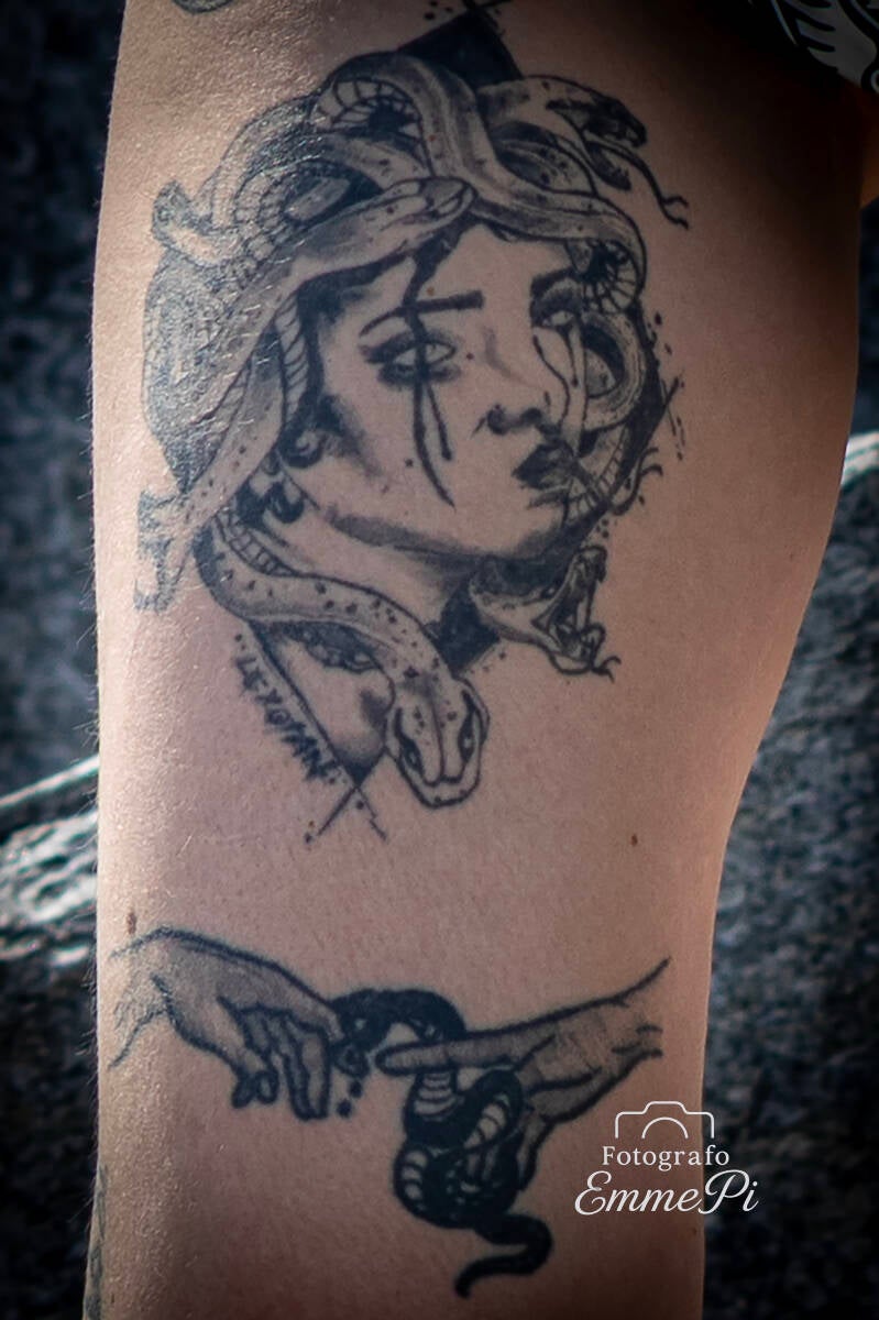 Primo piano di tatuaggio raffigurante un volto femminile intrecciato a serpenti sulla coscia.