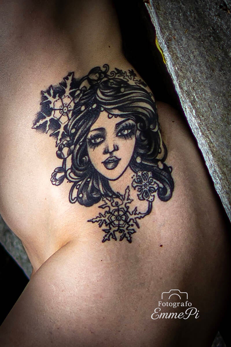 Primo piano di un tatuaggio femminile in stile illustrativo con fiocchi di neve e capelli scuri su un fianco illuminato in luce morbida.