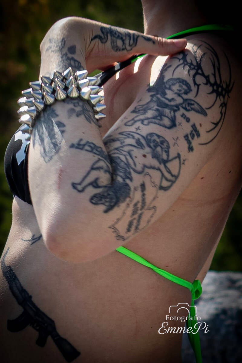 Dettaglio di tatuaggi su braccio femminile con figure stilizzate e bracciale borchiato metallico.