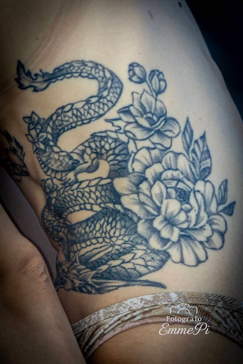 Primo piano di tatuaggio con serpente intrecciato a grandi fiori sul fianco femminile.