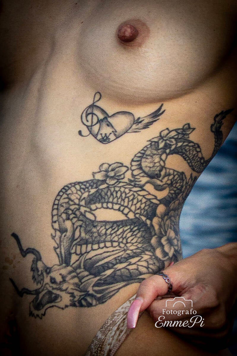 Composizione di tatuaggi con serpente, teschio e decorazioni floreali sul torso femminile in costume chiaro.