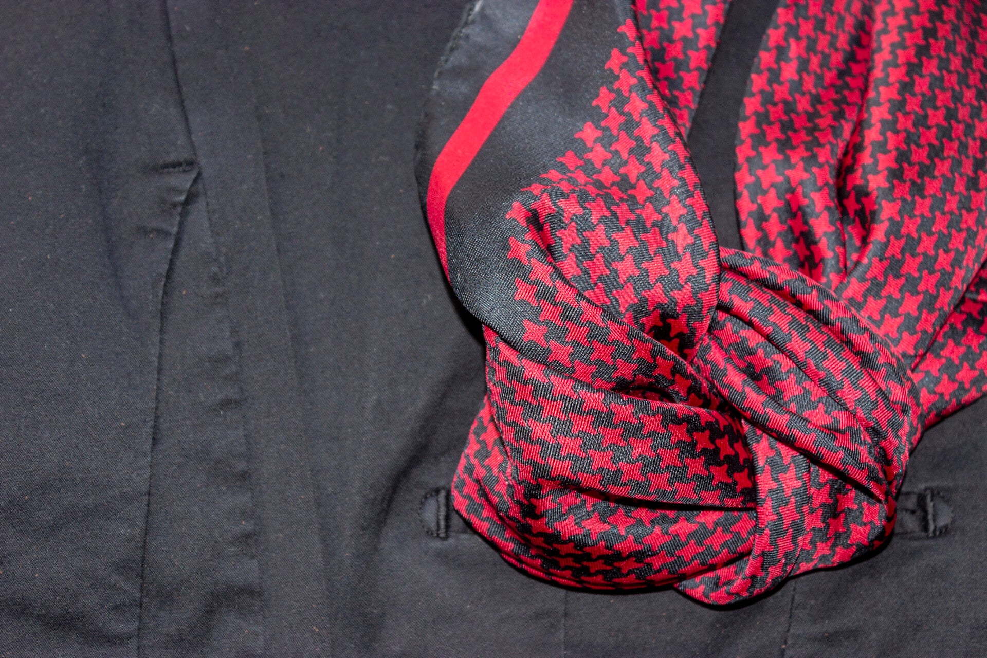 foulard maschile rosso e blu con motivo pied de poule, annodato e appoggiato su giacca blu elegante con tasca visibile