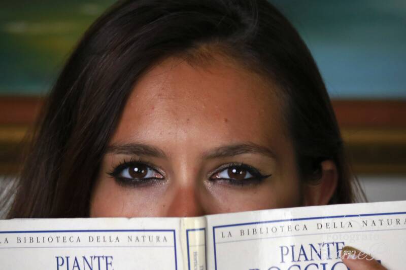 Primo piano di Dafne che guarda direttamente l'obiettivo lasciando visibili soltanto gli occhi sopra un libro aperto.