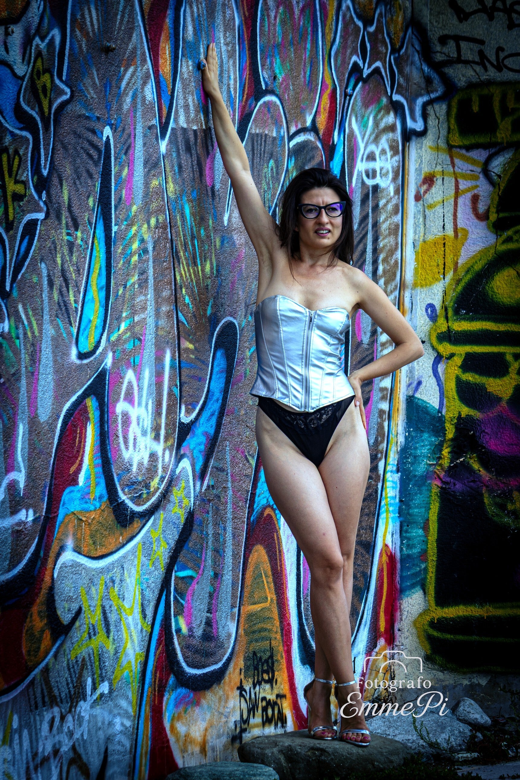 Marina posa con corsetto chiaro davanti a una parete ricoperta di graffiti colorati, in un ritratto artistico ambientato urbano.