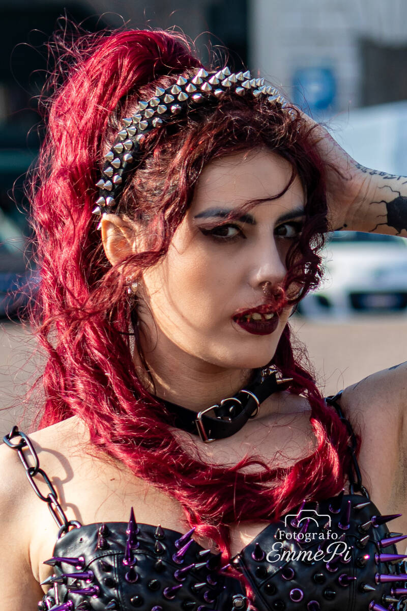 Donna con capelli rossi e accessori punk in primo piano, sguardo diretto e deciso.