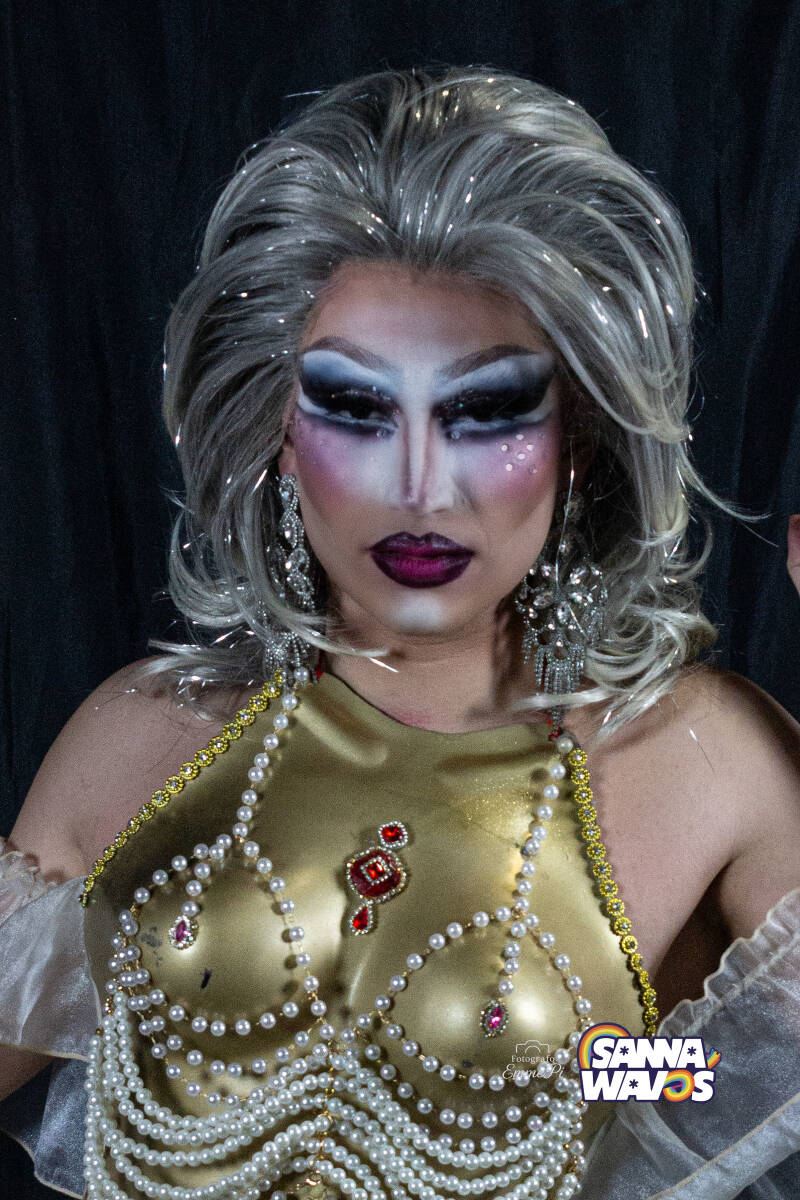 Ritratto di Robyn Goode, drag queen con trucco artistico e abito elegante, posa frontale intensa.