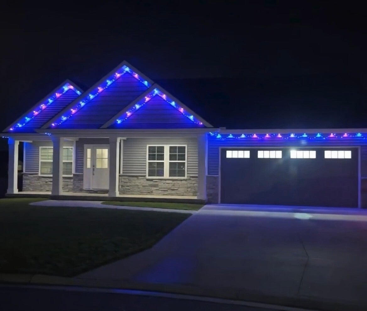 Professional permanent holiday lighting installation Cincinnati, featuring vibrant blue LED lights outlining the three gables and roofline of a modern gray home at night.