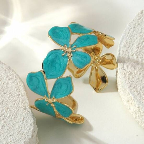Turquoise Bloemen Armband – Goudkleurige Statement Bangleit unieke ontwerp combineert een stralend zonmotief met verfijnde spiraaldetails, wat symbool staat voor energie, balans en tijdloze schoonheid.  De open cuff-structuur zorgt voor een co