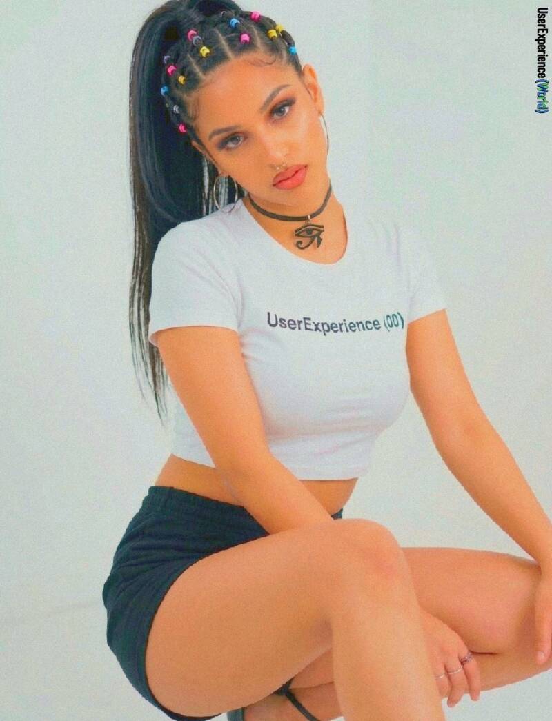 Music artist lil’ Keyah in a black-and-white studio portrait. She is wearing a white t-shirt that says "UserExperience(00)" and an Eye of Horus choker, with her hair in a high braided ponytail. photography by UserExperience (World) 