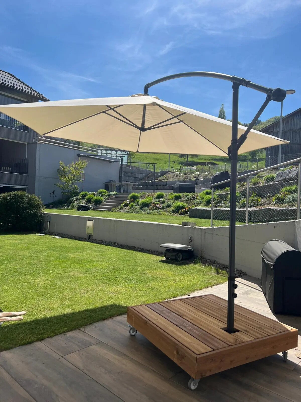 Fahrbarer-Sonnenschirm-Sockel mit einer Verkleidung aus imprägniertem Fichtenholz auf einer Terrasse.