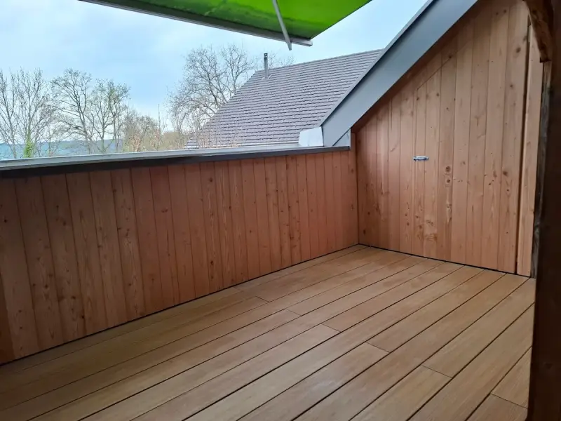 Hellbraune WPC-Terrassendielen auf einer Dachterrasse, kombiniert mit einer modernen Wandverkleidung aus Douglasie-Holz.