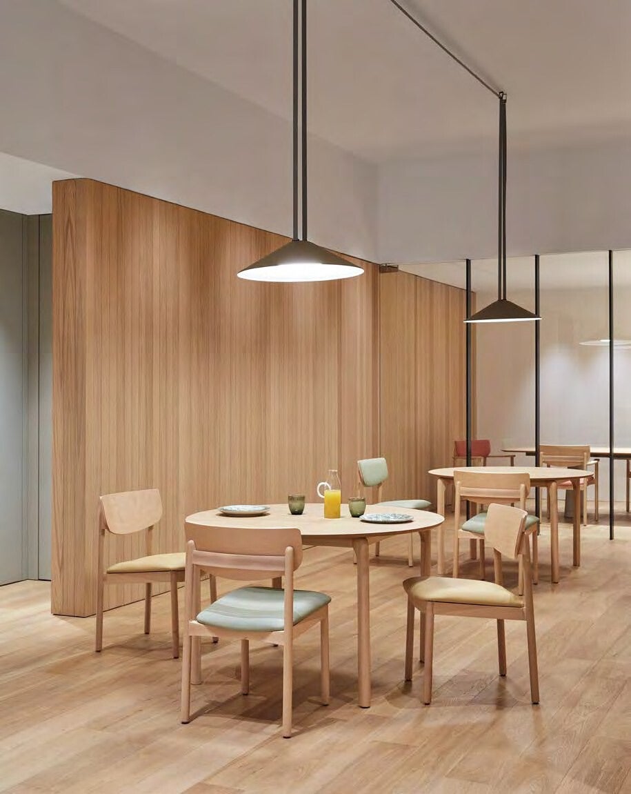 Espace repas chaleureux avec tables rondes et chaises en bois pour résidence seniors