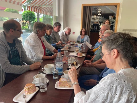 Dreizehn Personen am Tisch Kuchen, Eis, Kakao und Cafe verzehrend. Sie unterhalten sich angeregt