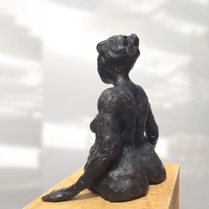 De achterkant van een bronzen beeld van een baadster  op een houten sokkel