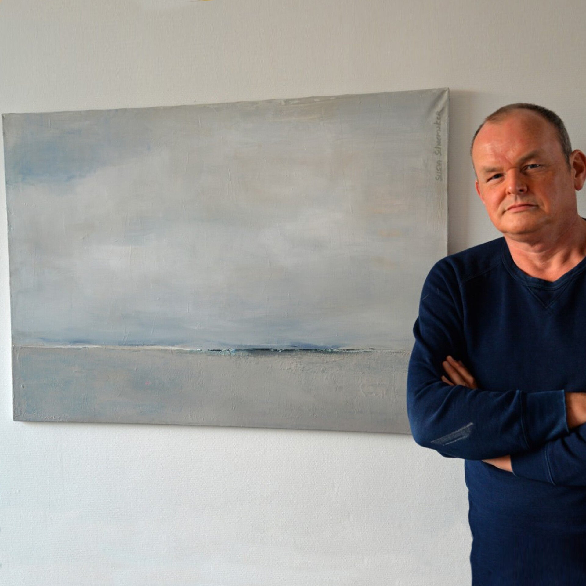 Stoere man staat voor een schilderij van een abstract landschap